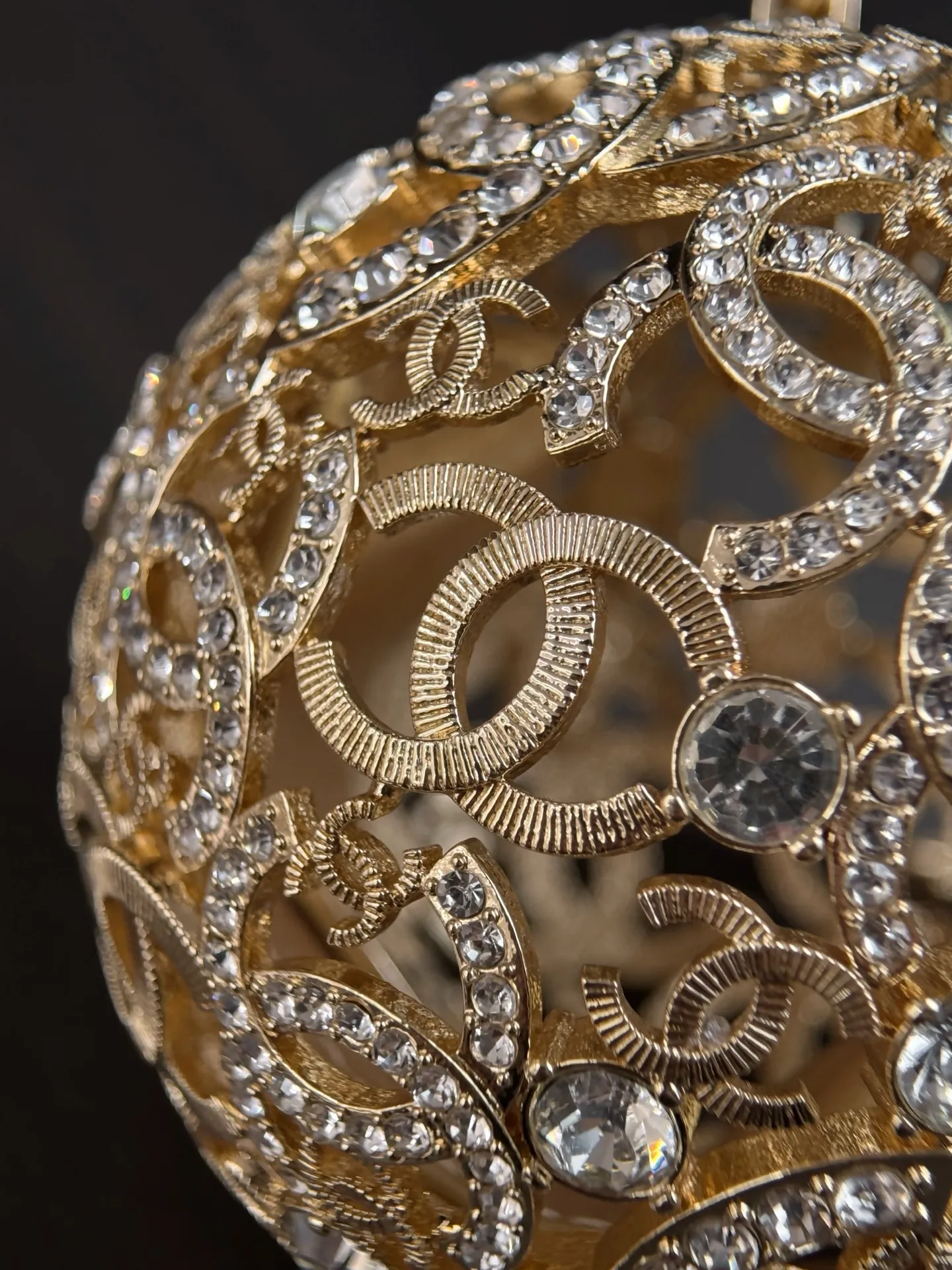 Chanel 25A 手工坊系列金色镂空球形晚宴包。 整只包是一颗金属球体, 巴洛克 风格的镂空花纹 + 漫天水钻镶嵌,中间嵌着双C Logo,链条肩带也是金色粗链设计,整体非常华丽复古。属于 Chanel 手工坊的收藏家级作品。 这种球形镂空金属工艺灵感来自传统香囊/挂坠的设计,搭配满钻之后更像一件可佩戴的艺术品。基本上是为了晚宴、红毯、派对这类重要场合而生,日常实用性几乎为零,但辨识度拉满。