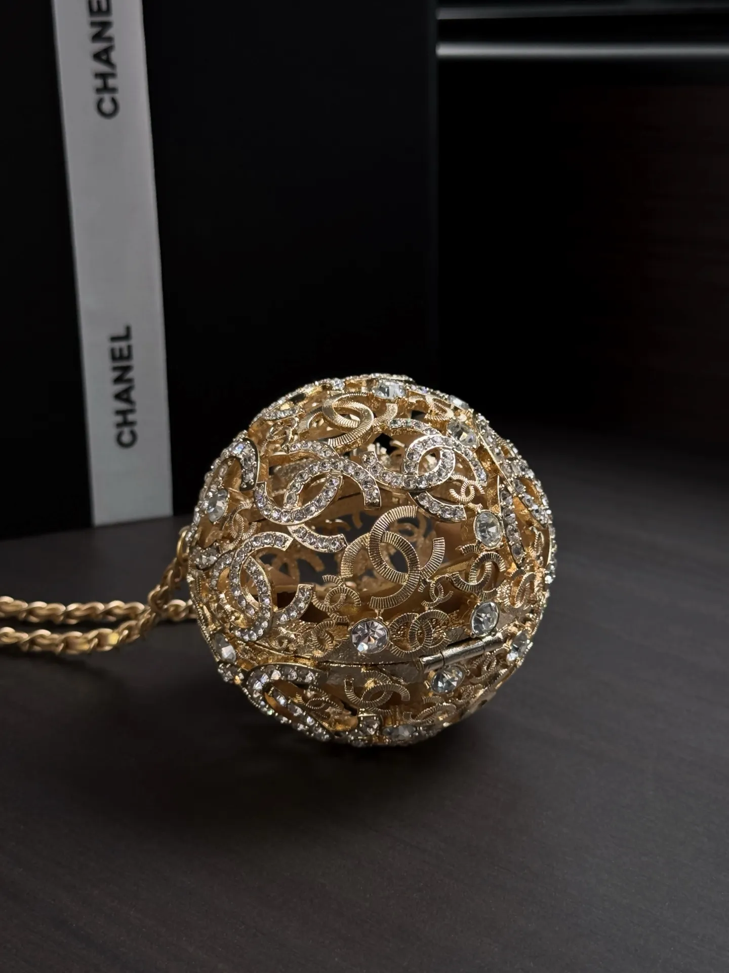 Chanel 25A 手工坊系列金色镂空球形晚宴包。 整只包是一颗金属球体, 巴洛克 风格的镂空花纹 + 漫天水钻镶嵌,中间嵌着双C Logo,链条肩带也是金色粗链设计,整体非常华丽复古。属于 Chanel 手工坊的收藏家级作品。 这种球形镂空金属工艺灵感来自传统香囊/挂坠的设计,搭配满钻之后更像一件可佩戴的艺术品。基本上是为了晚宴、红毯、派对这类重要场合而生,日常实用性几乎为零,但辨识度拉满。