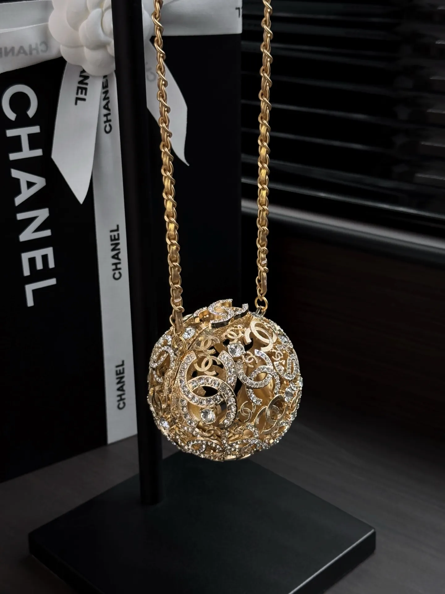 Chanel 25A 手工坊系列金色镂空球形晚宴包。 整只包是一颗金属球体, 巴洛克 风格的镂空花纹 + 漫天水钻镶嵌,中间嵌着双C Logo,链条肩带也是金色粗链设计,整体非常华丽复古。属于 Chanel 手工坊的收藏家级作品。 这种球形镂空金属工艺灵感来自传统香囊/挂坠的设计,搭配满钻之后更像一件可佩戴的艺术品。基本上是为了晚宴、红毯、派对这类重要场合而生,日常实用性几乎为零,但辨识度拉满。
