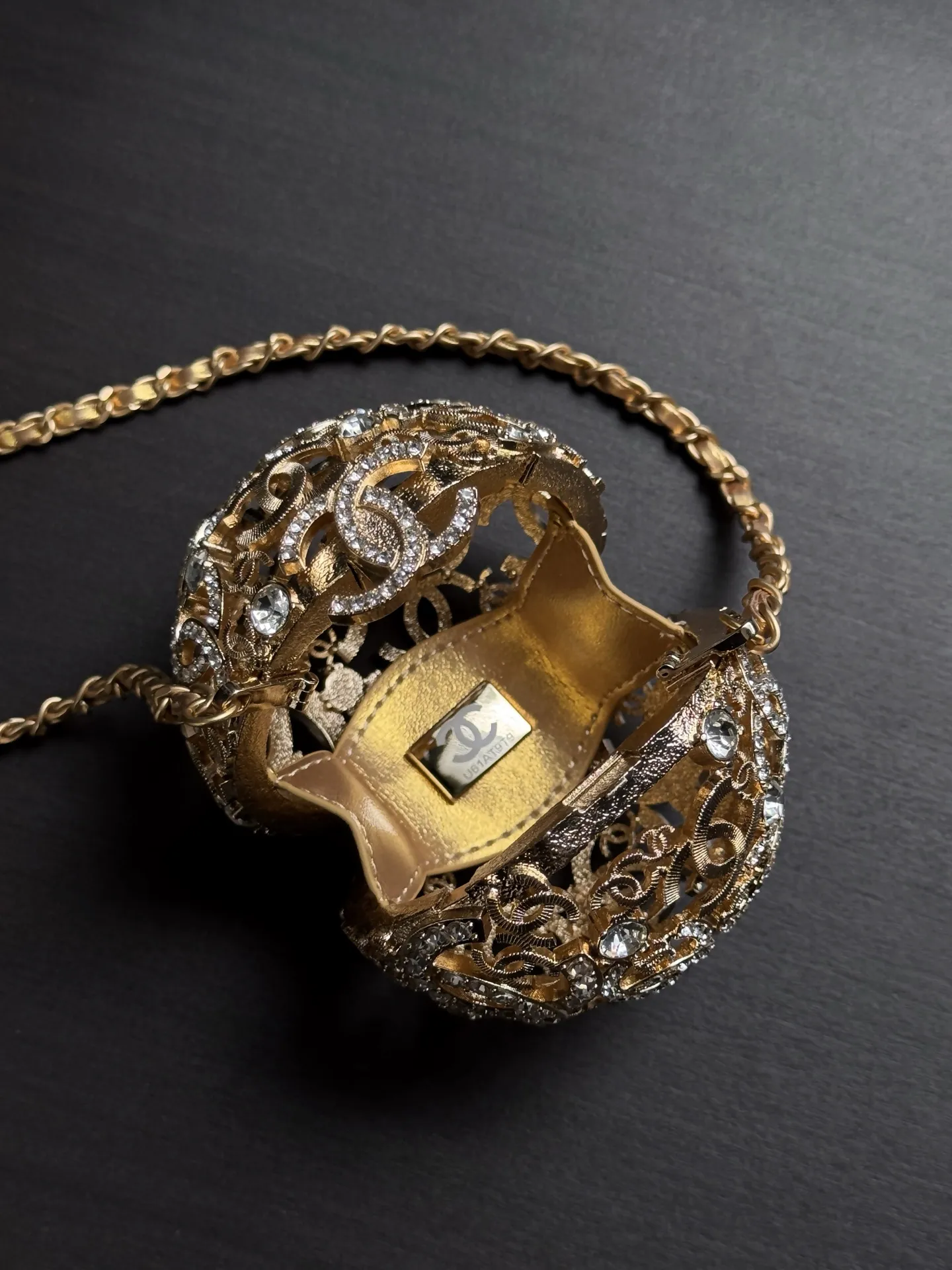 Chanel 25A 手工坊系列金色镂空球形晚宴包。 整只包是一颗金属球体, 巴洛克 风格的镂空花纹 + 漫天水钻镶嵌,中间嵌着双C Logo,链条肩带也是金色粗链设计,整体非常华丽复古。属于 Chanel 手工坊的收藏家级作品。 这种球形镂空金属工艺灵感来自传统香囊/挂坠的设计,搭配满钻之后更像一件可佩戴的艺术品。基本上是为了晚宴、红毯、派对这类重要场合而生,日常实用性几乎为零,但辨识度拉满。