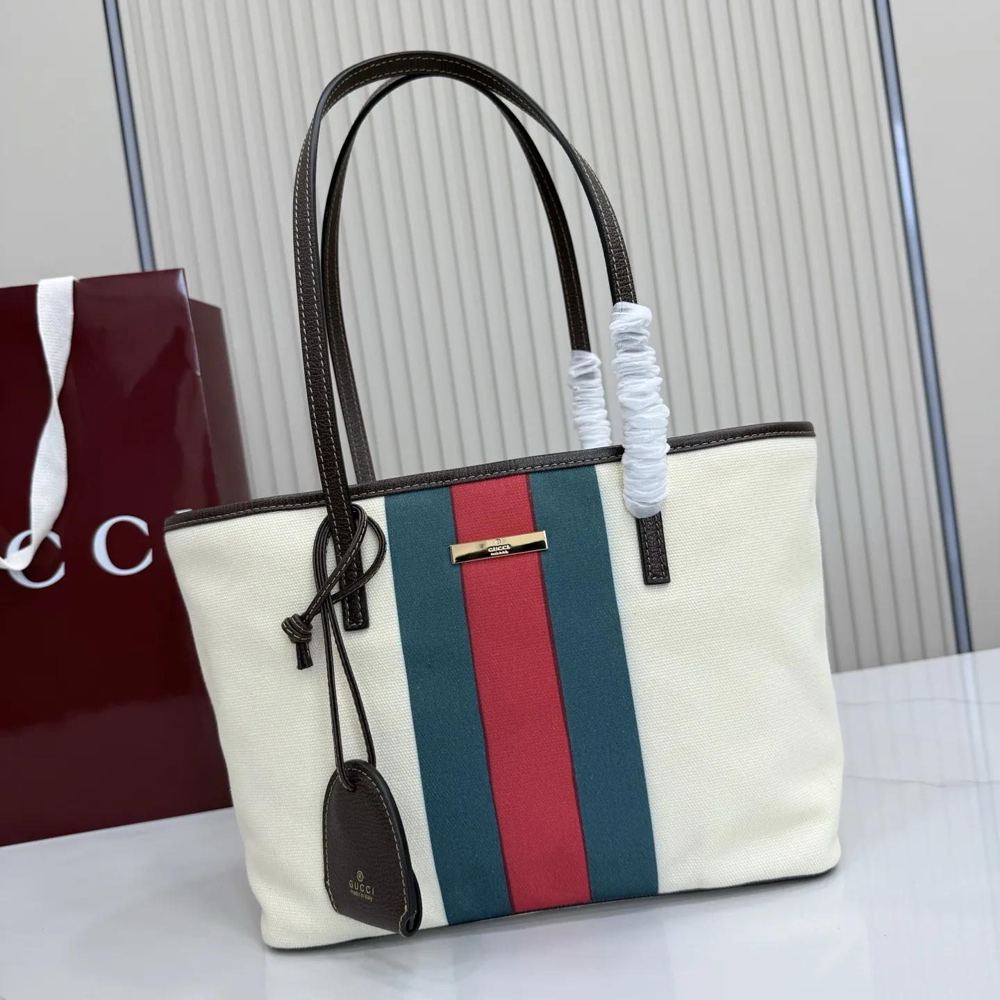 p480。【配全套包装】‼️Generation Gucci系列深入探索品牌典藏元素,将不同世代的设计融入一体,营造出独特的美学叙事。水洗GG帆布为精致廓形增添品牌标识性细节,如这款托特包,通过魅力装饰和品牌标识徽牌,将日常风格提升至新高度。 天然水洗帆布 棕色皮革滚边 金色调配件 棕色皮革吊饰 米色和深棕色棉质衬里 提手下垂:23厘米 饰按扣闭合 型号:A0034E。 尺寸:25厘米(宽)x 19厘米(高)x 11.5厘米(深) 重量:约260克 颜色:棕色/帆布。 意大利创作