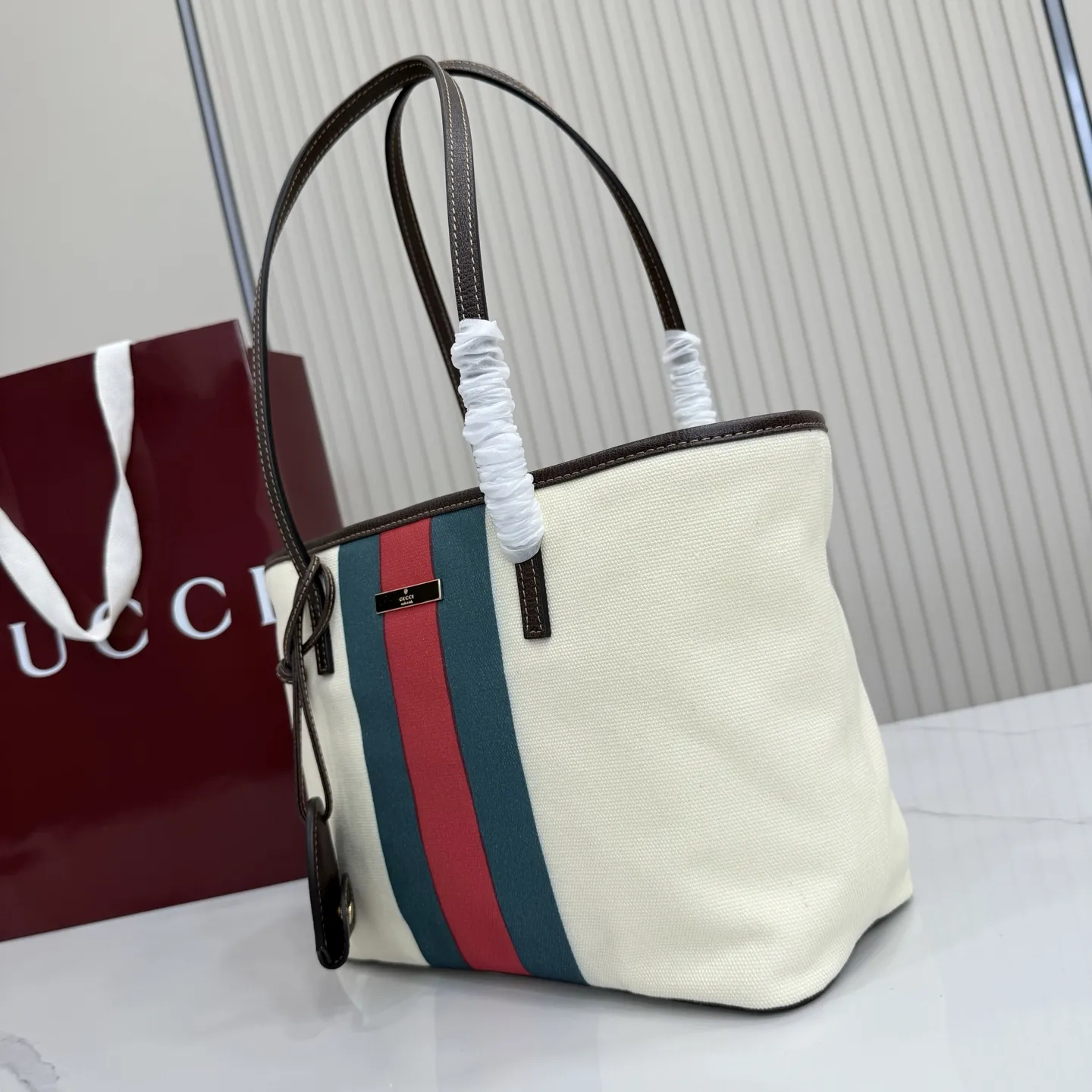p480。【配全套包装】‼️Generation Gucci系列深入探索品牌典藏元素，将不同世代的设计融入一体，营造出独特的美学叙事。水洗GG帆布为精致廓形增添品牌标识性细节，如这款托特包，通过魅力装饰和品牌标识徽牌，将日常风格提升至新高度。 天然水洗帆布 棕色皮革滚边 金色调配件 棕色皮革吊饰 米色和深棕色棉质衬里 提手下垂：23厘米 饰按扣闭合 型号：A0034E。 尺寸：25厘米（宽）x 19厘米（高）x 11.5厘米（深） 重量：约260克 颜色：棕色/帆布。 意大利创作