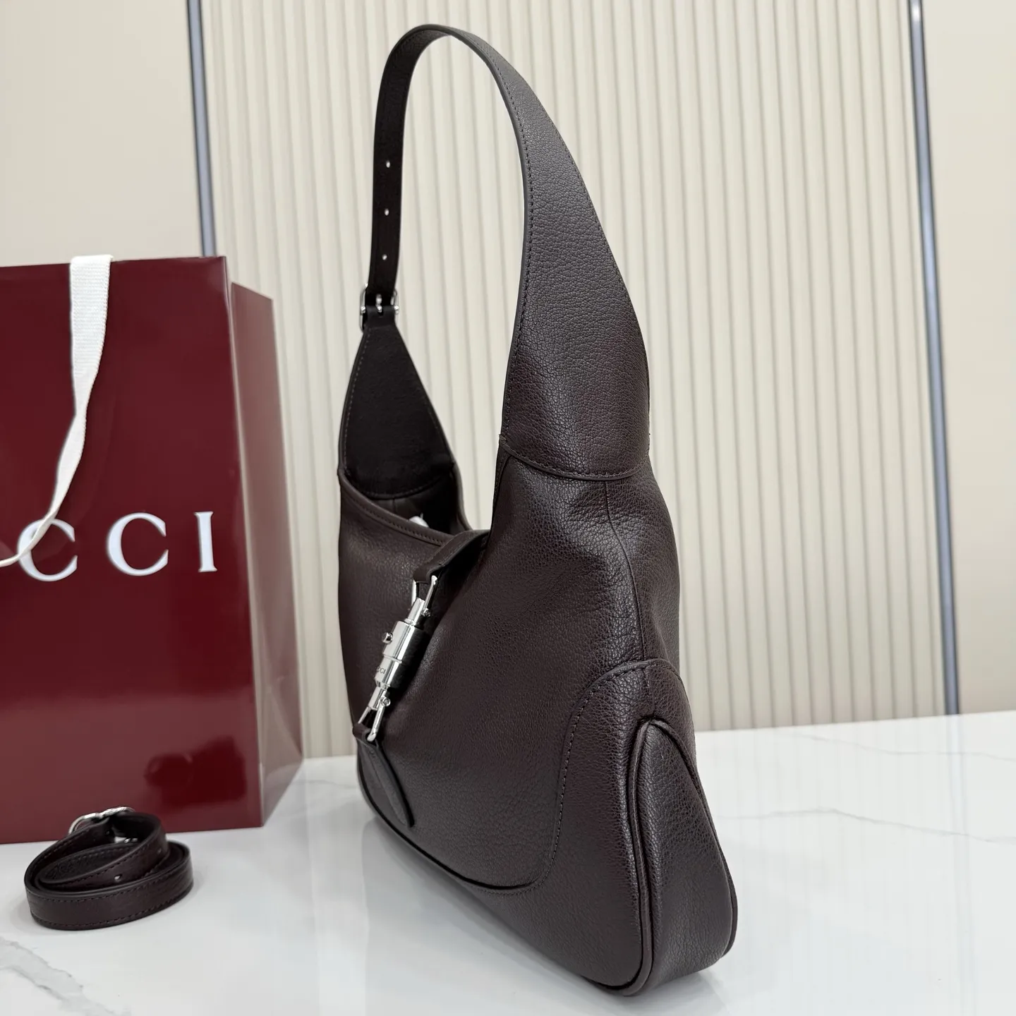 p750。【配全套包装】‼️(羊皮)2026春夏系列全新上市。这款Gucci Jackie 9161系列手袋呈现时髦风格,选用柔软粒面羊皮革,经手工悉心做旧处理,呈现出复古质感。手袋搭配便于使用的推入式锁扣设计,金色调金属配件更添品牌标志性五金细节的风格魅力。 型号:863136。 尺寸:31.5厘米(宽)x 22厘米(高)x 4.5厘米(深) 重量:约0.35千克 颜色:深棕色/羊皮。