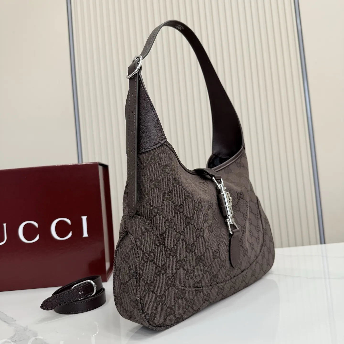 p530。【配全套包装】‼️2026春夏系列全新上市。这款Gucci Jackie 1961系列手袋在《La Famiglia》系列的&rdquo;La It Girl&ldquo;造型种呈现。包身选用轻盈但结构挺括的GG帆布，演绎复古灵感的沙色，搭配便于使用的金色调推入式锁扣设计，更添品牌魅力。 深棕色GG帆布 深棕色软皮皮革滚边 银色调配件 深棕色帆布衬里，饰钻石菱格纹图案 内部：1个拉链口袋 可调节提手长度：25 - 29cm 可调节延长肩带高：48 - 61cm 饰推入式锁扣 型号：863136。 尺寸：31.5厘米（宽）x 22厘米（高）x 4.5厘米（深） 重量：约0.35千克 颜色：深棕色/帆布。 意大利创作